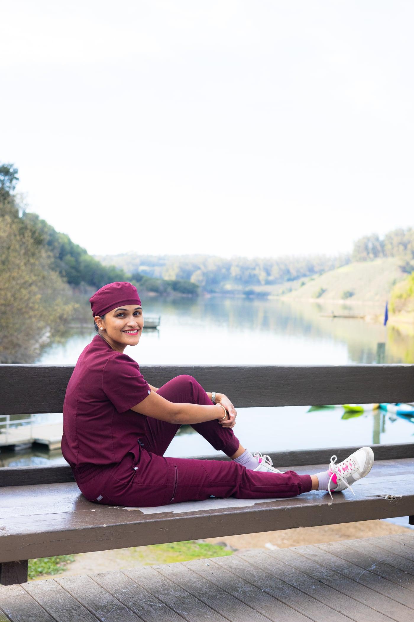 Dr. Sampada Deshpande seated by a lake in burgundy dental scrubs